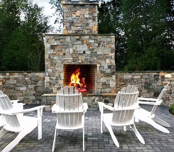 Outdoor stone fireplace with white chairs arranged around the hearth
