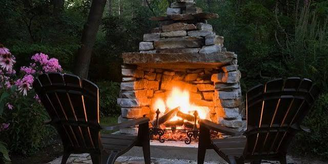 Rustic stone fireplace glowing beside two garden chairs