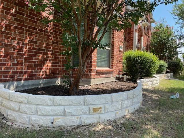 Curved white limestone flower bed beside a brick home