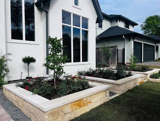 Raised stone planters with pale caps beside a modern home